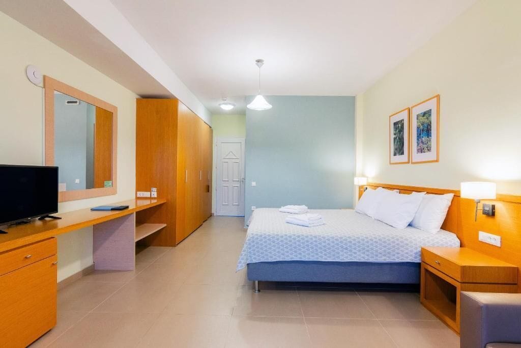 Ein Hotelzimmer mit Bett, Nachttisch, Fernseher, Kleiderschrank und Spiegel.