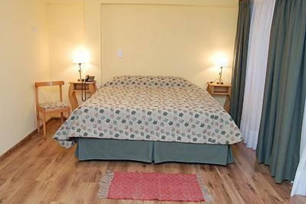 A bedroom with a bed, two bedside tables, a chair, a red rug, and curtains.