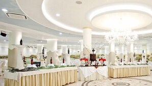 Un amplio salón de banquetes elegantemente decorado, con techos altos, candelabros y columnas blancas.