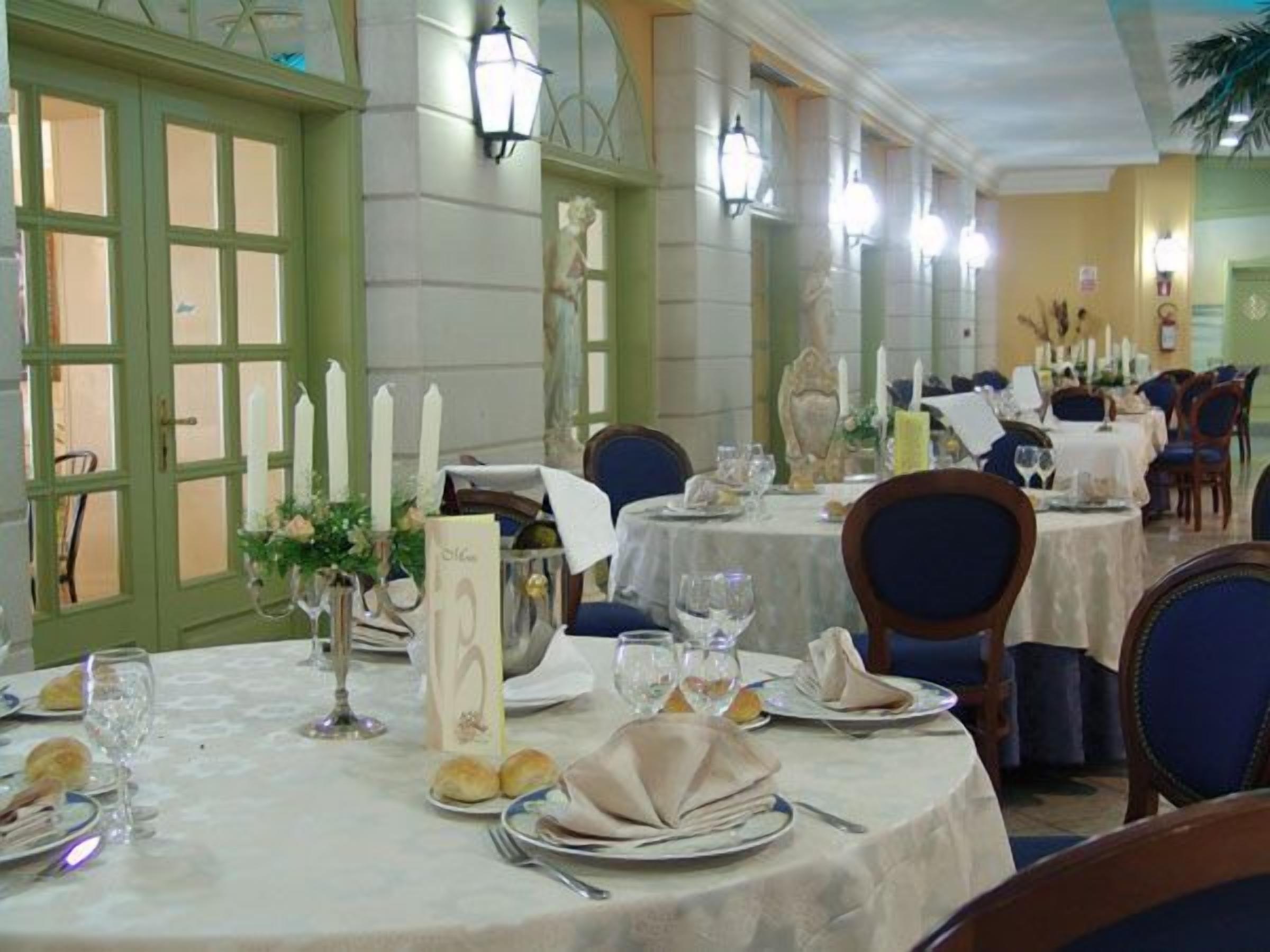 Un comedor con mesas redondas dispuestas para una comida, con manteles blancos, platos y cubiertos.