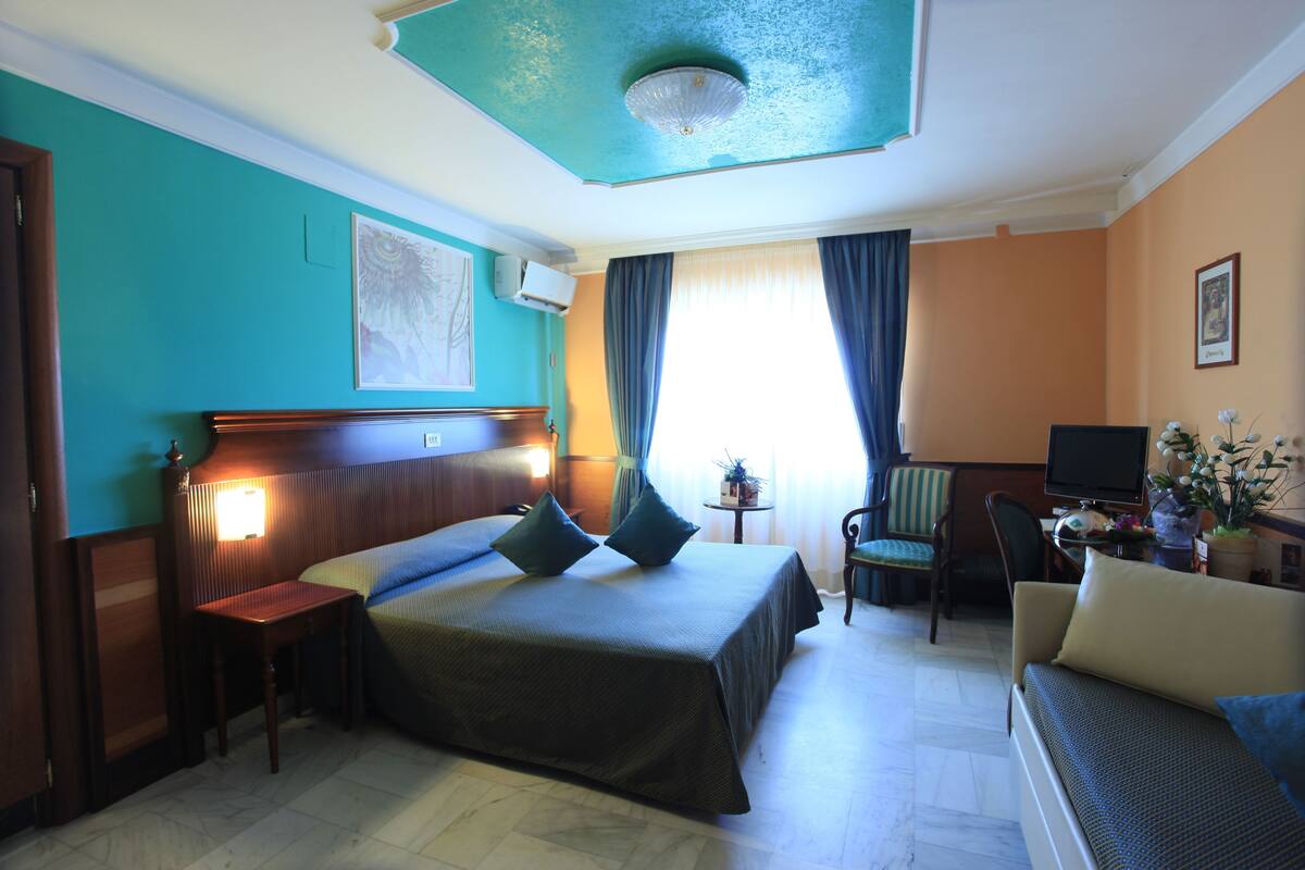 A hotel room with a bed, a desk, a chair, a television, and a window with curtains.
