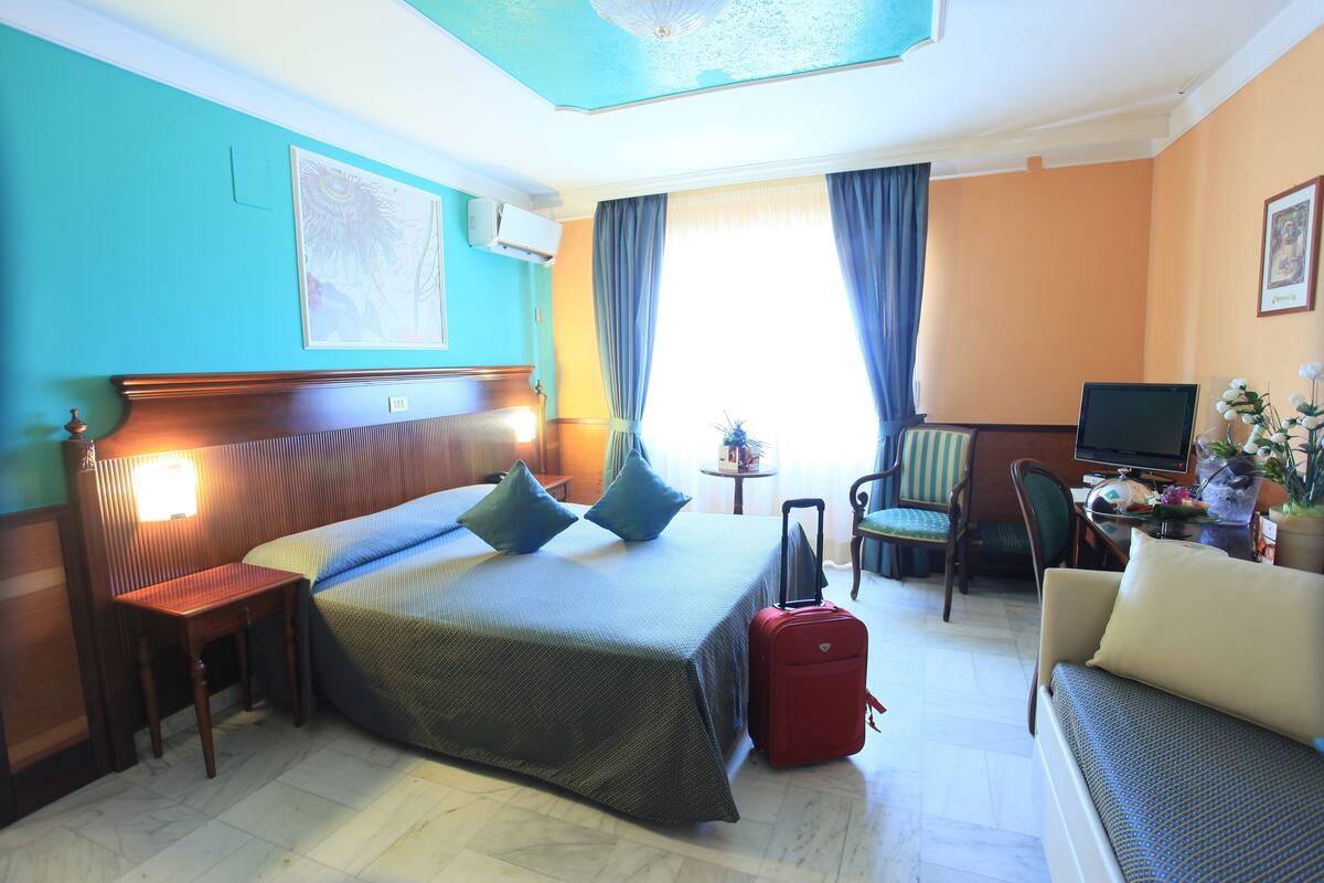 A hotel room with a bed, a desk, a chair, a sofa, and a TV.