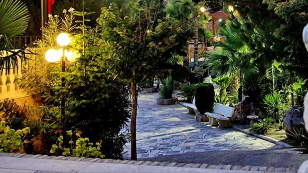 Un sendero de jardín con bancos, una estatua y abundante vegetación.
