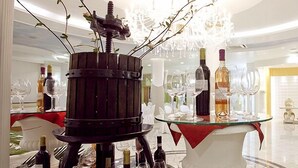 Un interior luminoso y elegante con una exhibición central de botellas de vino y copas, rodeado de sillas y mesas blancas.