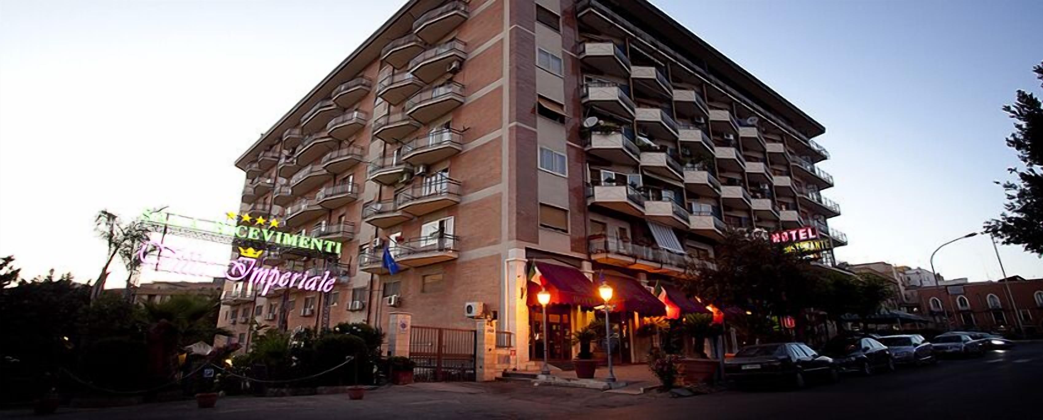A multi-story hotel with balconies, a restaurant with outdoor seating, and a visible sign for 'Imperiale'.