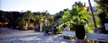 Un patio empedrado con bancos de piedra, palmeras y estatuas.