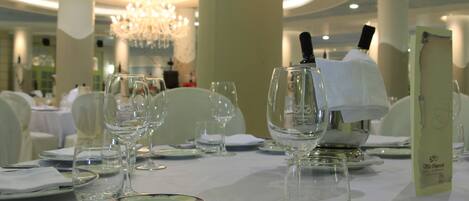 Una mesa de comedor elegantemente dispuesta con cristalería transparente, platos y cubiertos, y un atril para el menú en un ambiente formal.