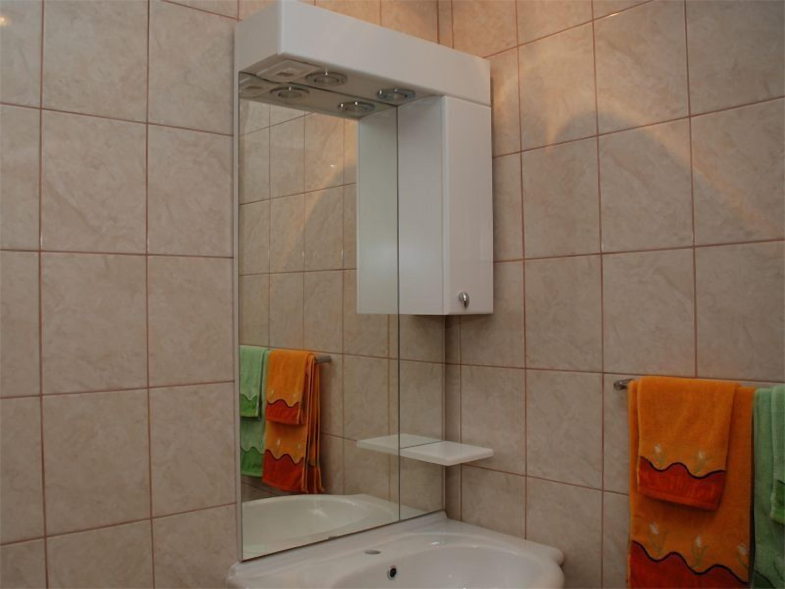 Une salle de bain avec un lavabo blanc, un meuble à miroir et des murs carrelés.