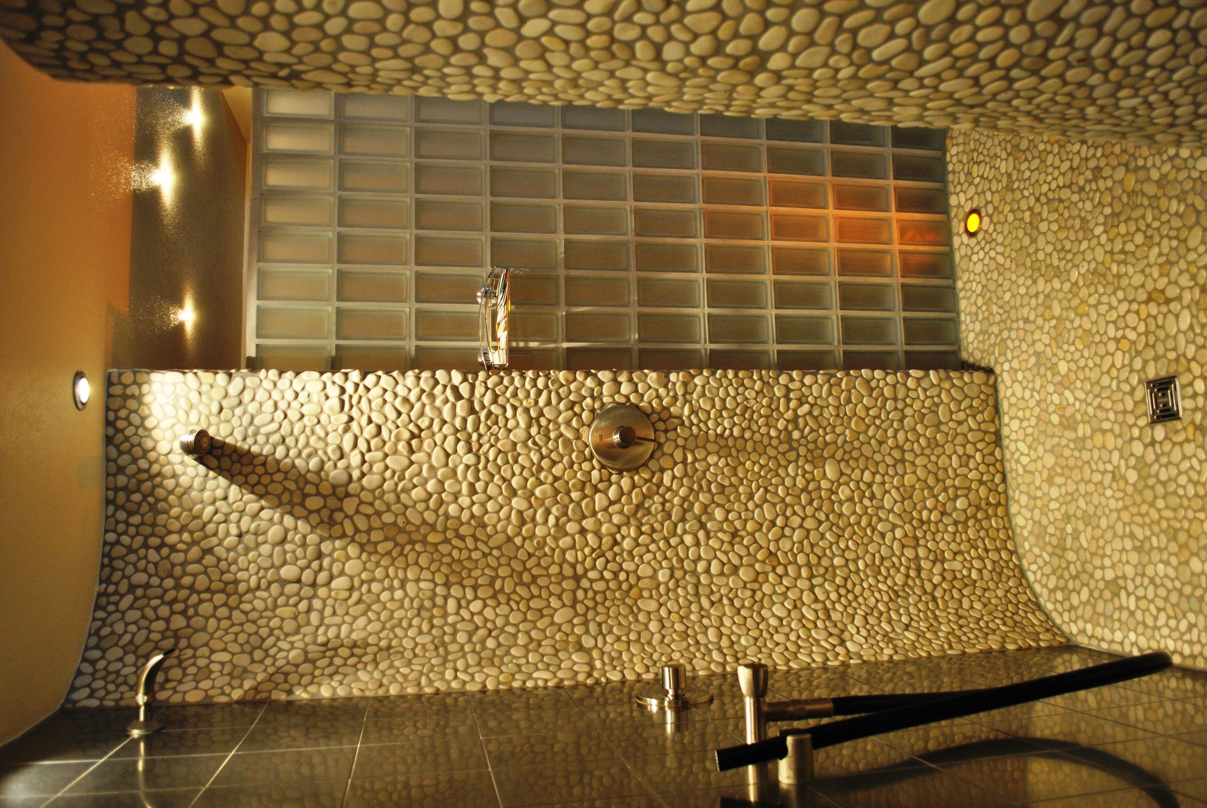 A bathroom with a pebble-patterned wall, a glass block window, and a modern faucet.