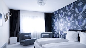 Une chambre d’hôtel moderne avec un grand lit, deux fauteuils, une petite table et un crâne décoratif accroché au mur.