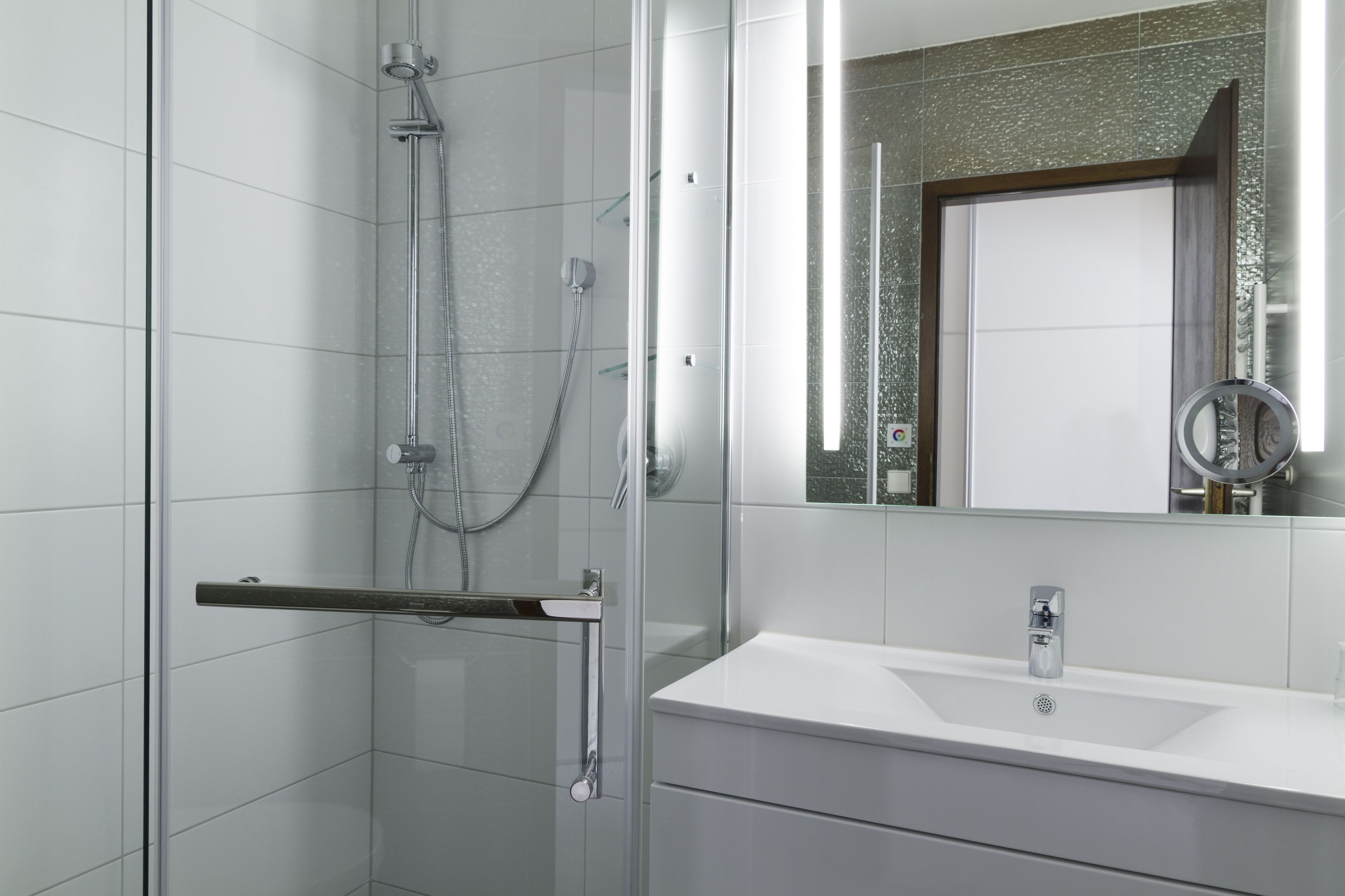 Une salle de bain moderne avec une douche à parois de verre, un lavabo blanc et un grand miroir doté d’un cadre décoratif.