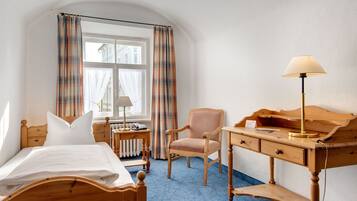 A hotel room with a bed, a desk, a chair, a lamp, and a window with curtains.