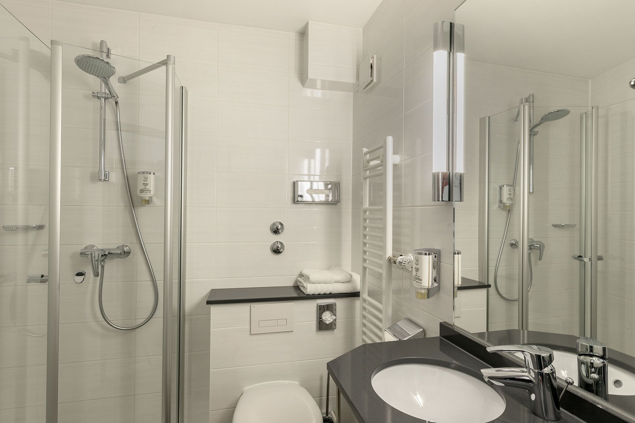 A modern bathroom with a glass-enclosed shower, a white toilet, and a black countertop with a sink and mirror.