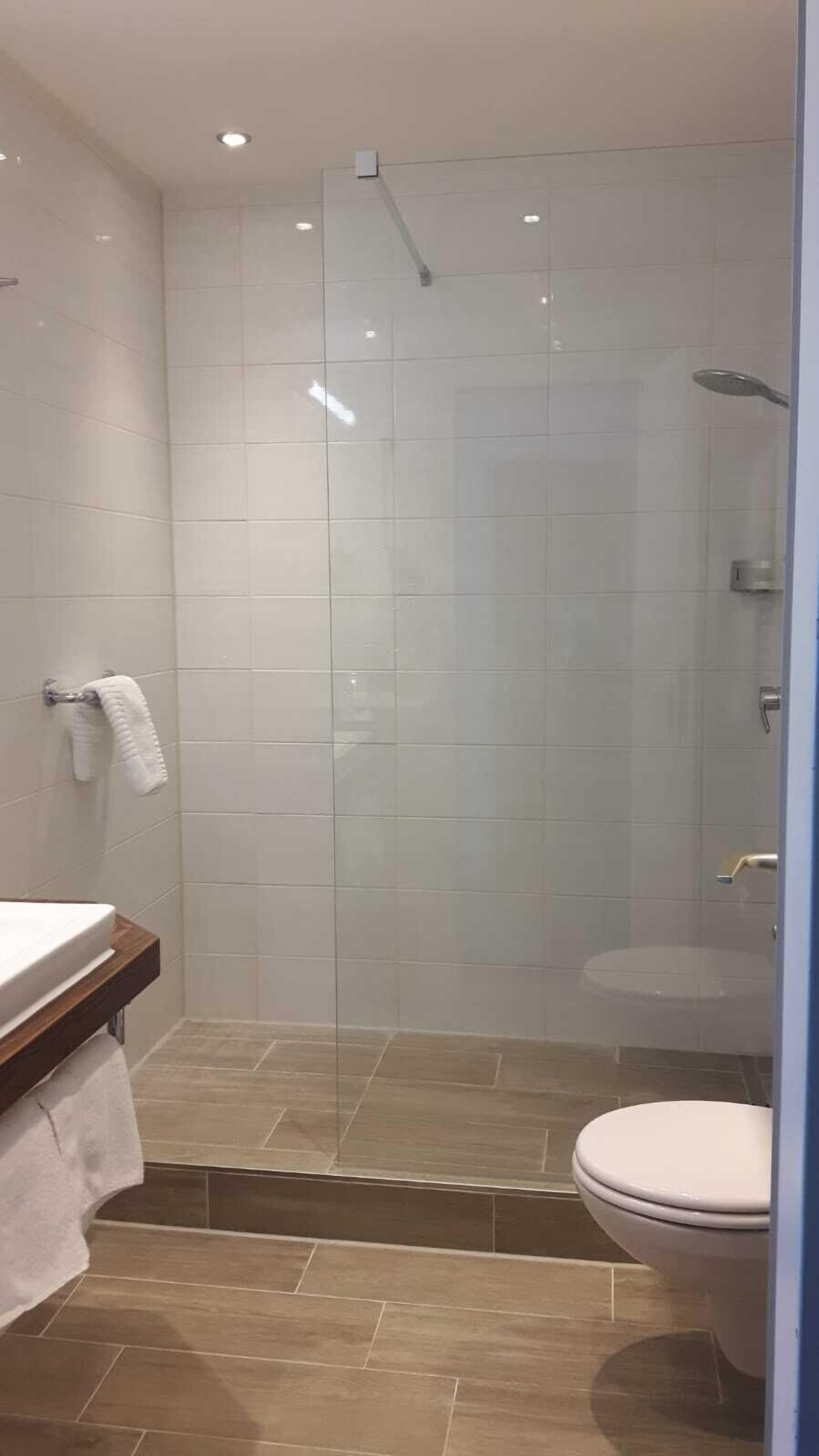 A modern bathroom with a glass-enclosed shower, a toilet, and a sink with a towel rack.