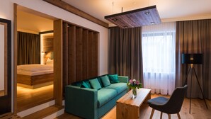 A modern hotel room with a wooden ceiling, a green sofa, a wooden coffee table, and a black floor lamp. - KOLBERBRÄU Posthotel und Gasthaus (Bad Toelz)