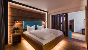 A modern bedroom with a wooden headboard, a bedside table with a vase of flowers, and a large bed with white linens. - KOLBERBRÄU Posthotel und Gasthaus (Bad Toelz)
