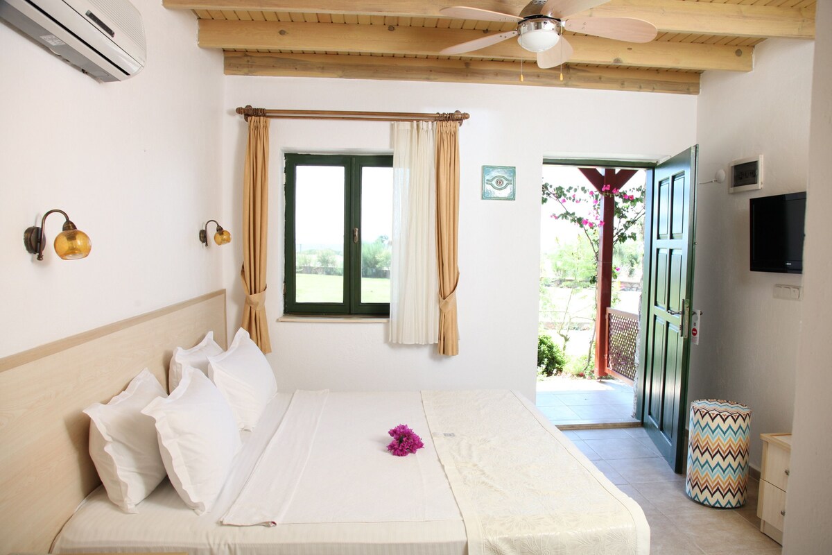 A bedroom with a bed, curtains, a ceiling fan, an air conditioner, a television, and a view of the outside.