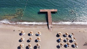 An aerial view of a beach with a wooden pier extending into the water, surrounded by sun loungers and umbrellas. - Flow Datca Surf & Beach Hotel (Datça)
