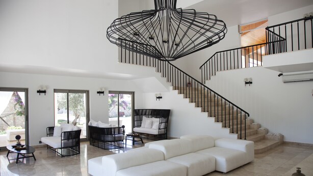 A spacious living area with a large white sectional sofa, a black wicker sofa, and a coffee table. A modern black staircase with a unique metal design leads to an upper level. - Flow Datca Surf & Beach Hotel (Datça)