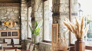 A rustic dining area with stone walls, wooden furniture, and large windows. - Flow Datca Surf & Beach Hotel (Datça)