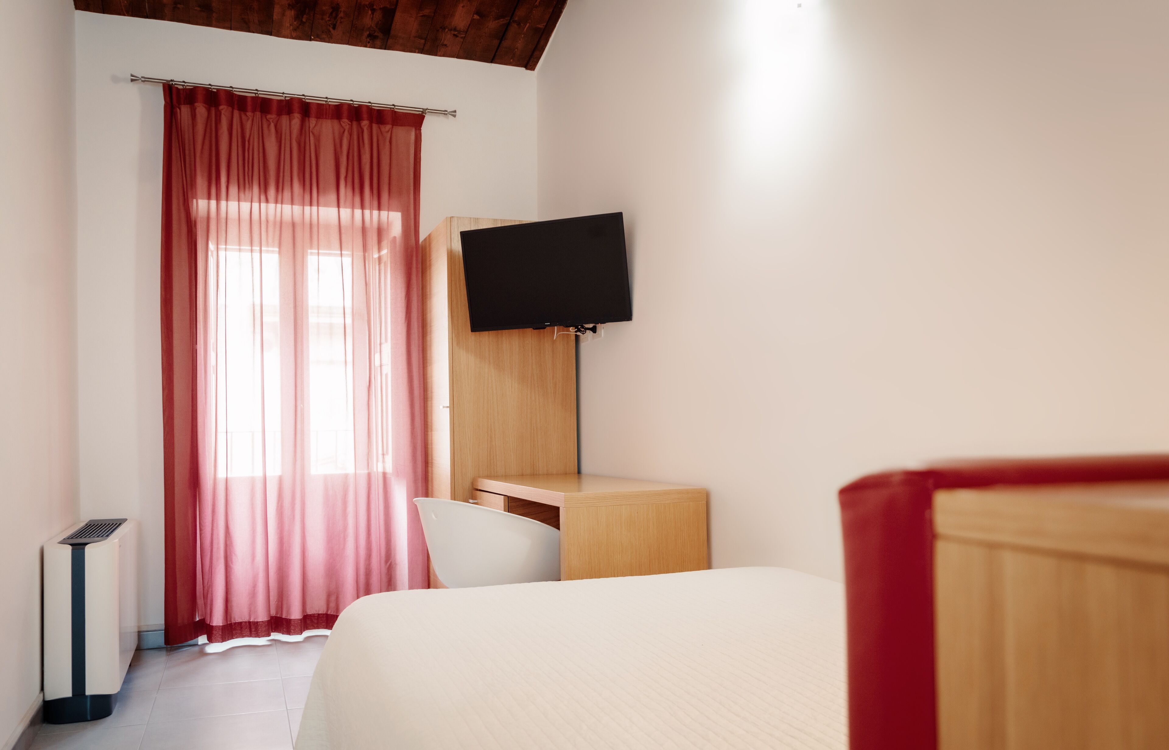 Een slaapkamer met een bed, een bureau, een stoel, een televisie en een raam met gordijnen.