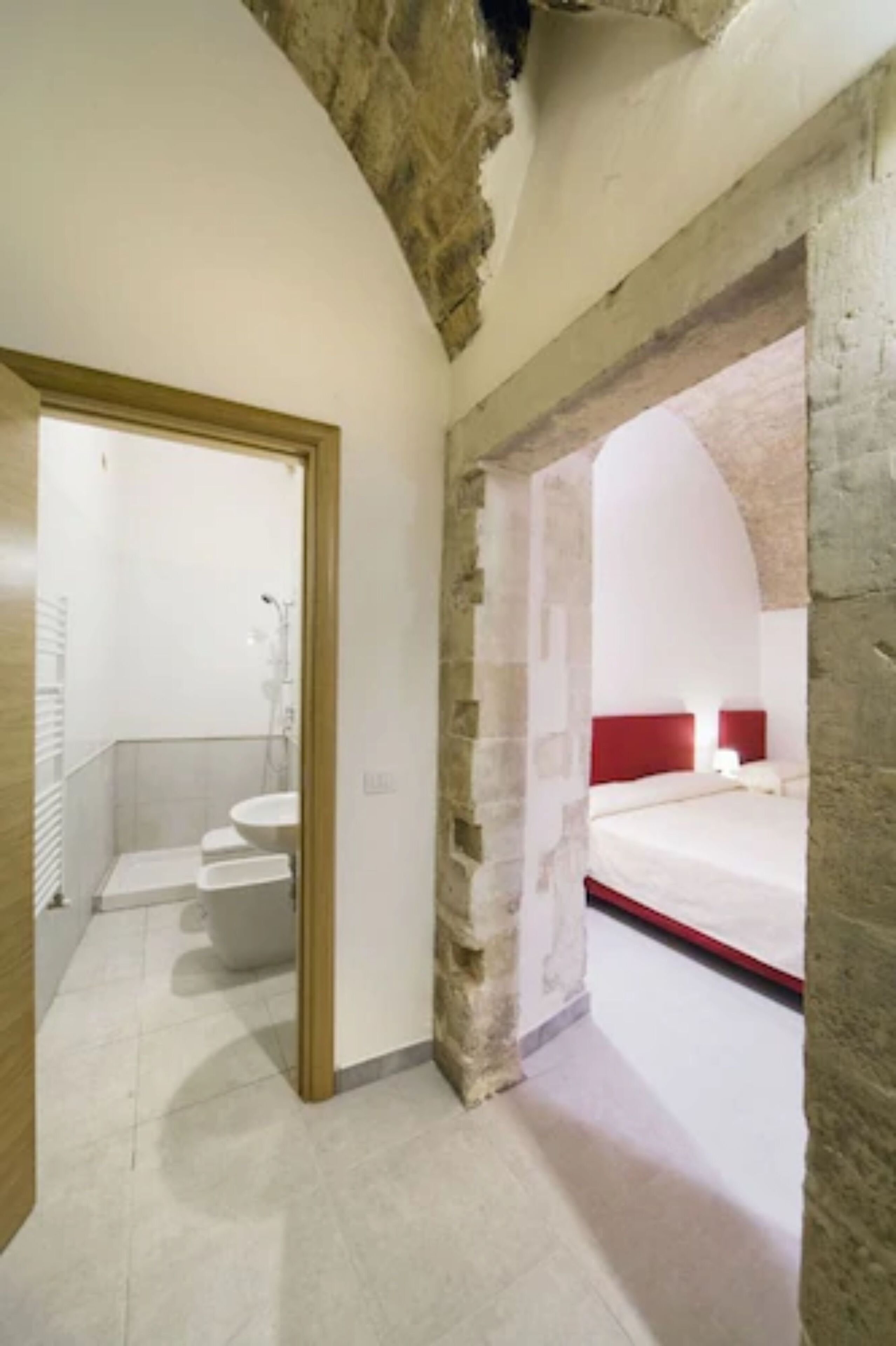 A modern hotel room with a stone archway leading to a bathroom with a white sink and shower.
