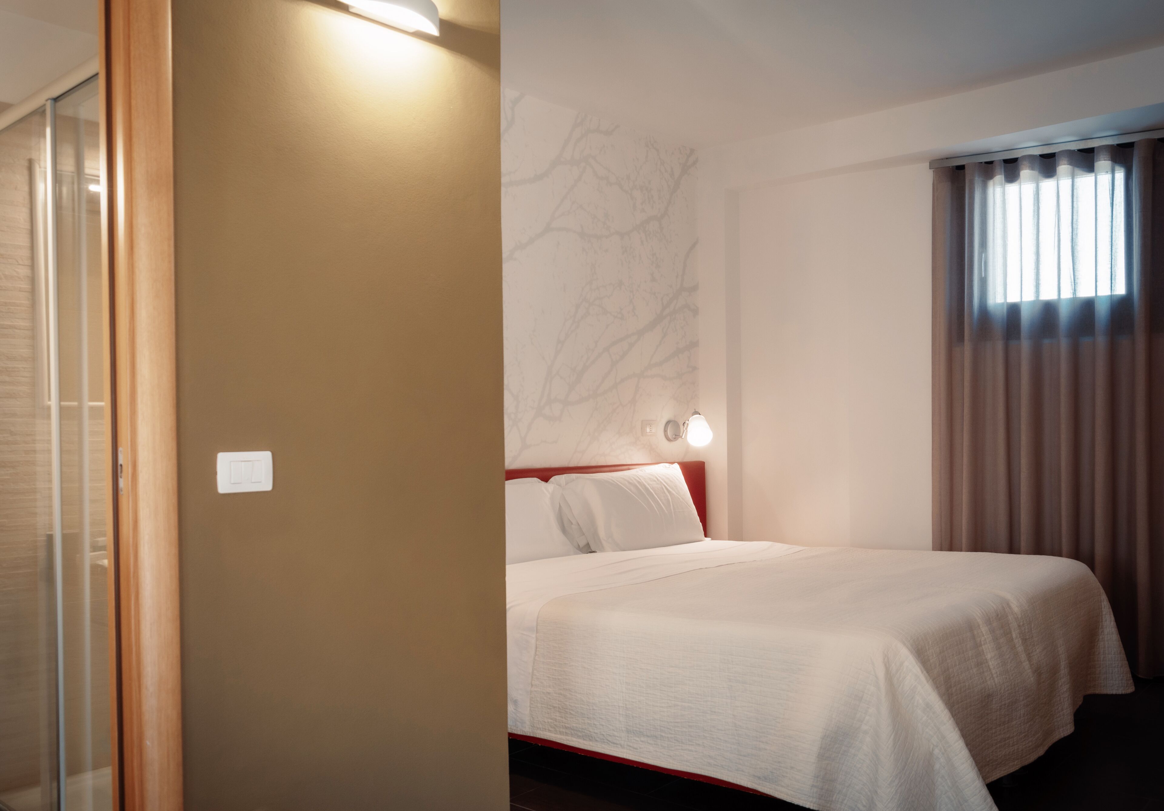 Una habitación de hotel con una cama, una lámpara de pared y un ventanal con cortinas.