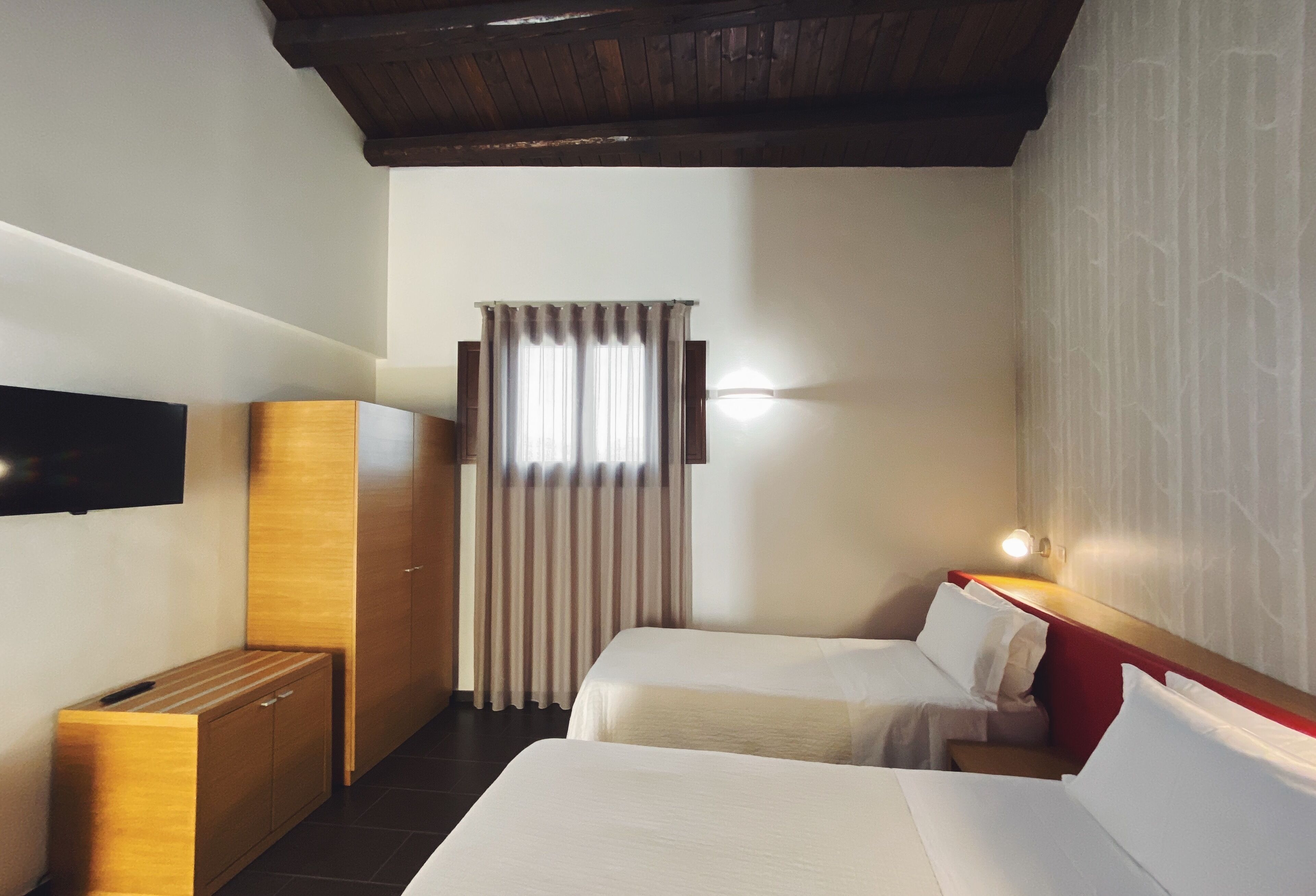 A hotel room with two beds, a wooden cabinet, a TV, and a window with curtains.