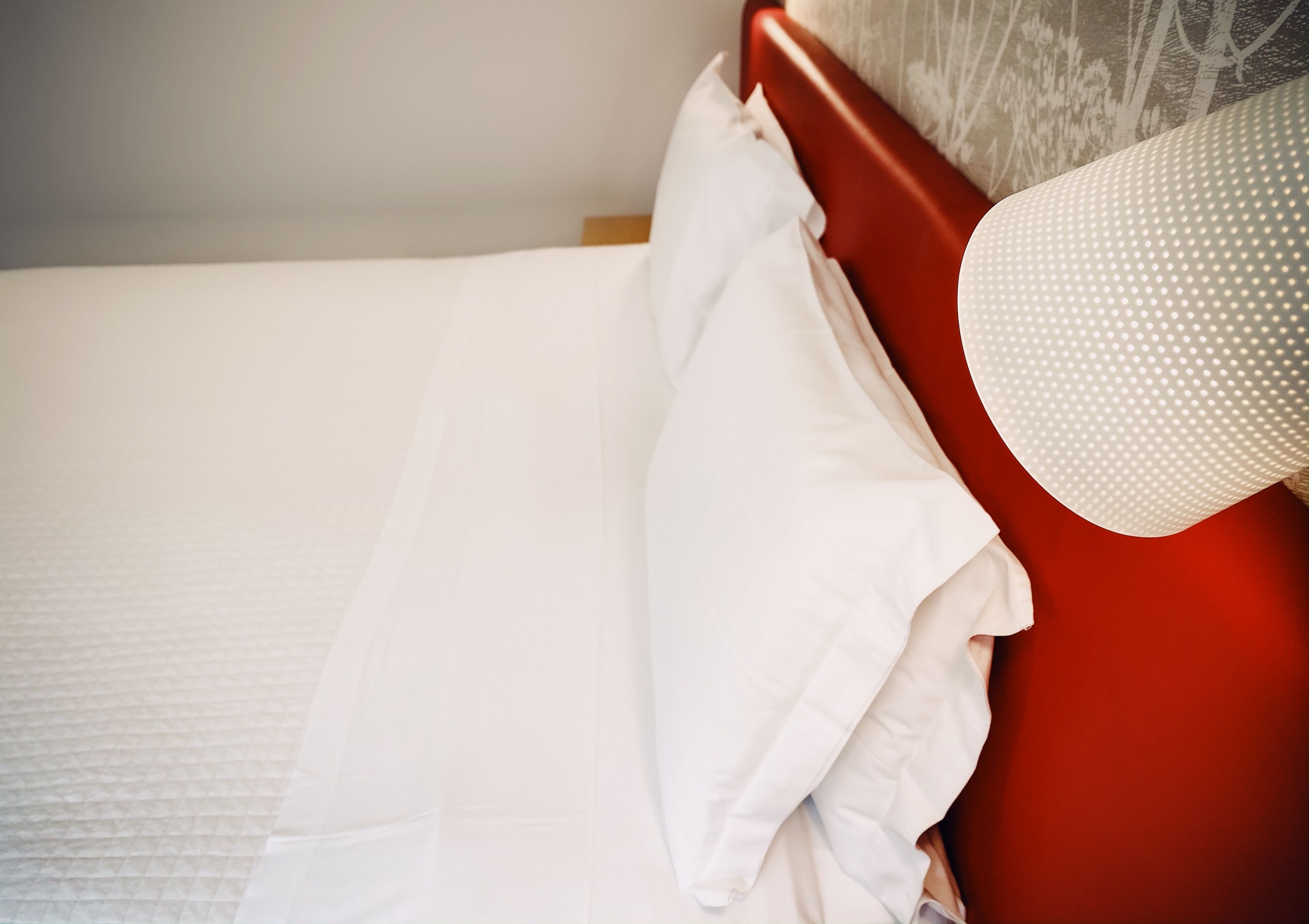 A bed with white bedding and a red headboard.