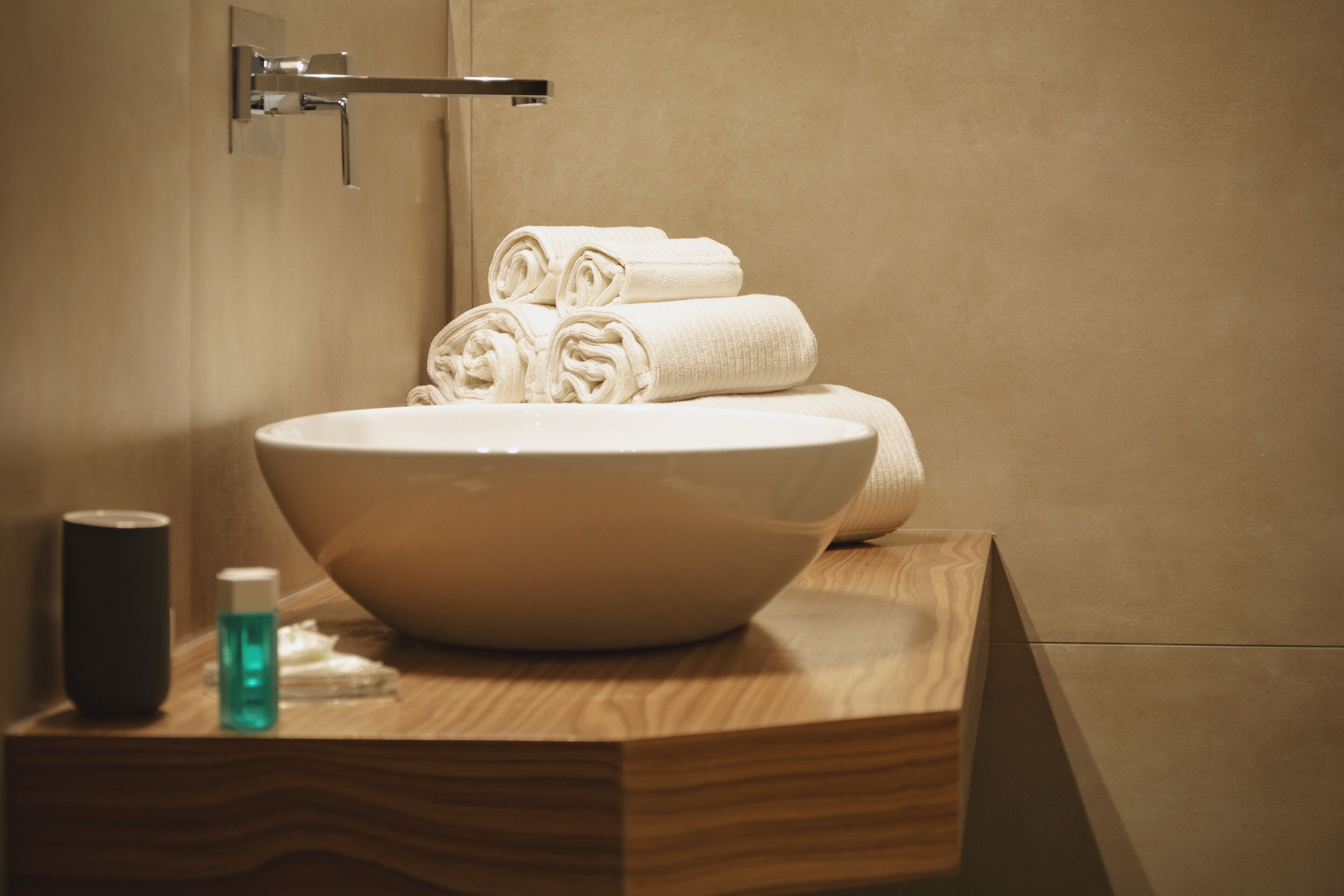 Un baño con un lavamanos grande de color blanco, encimera de madera y toallas enrolladas con cuidado.