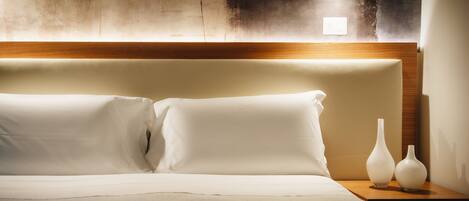 A neatly made bed with white linens, two white vases on a bedside table, and a textured wall behind the bed.