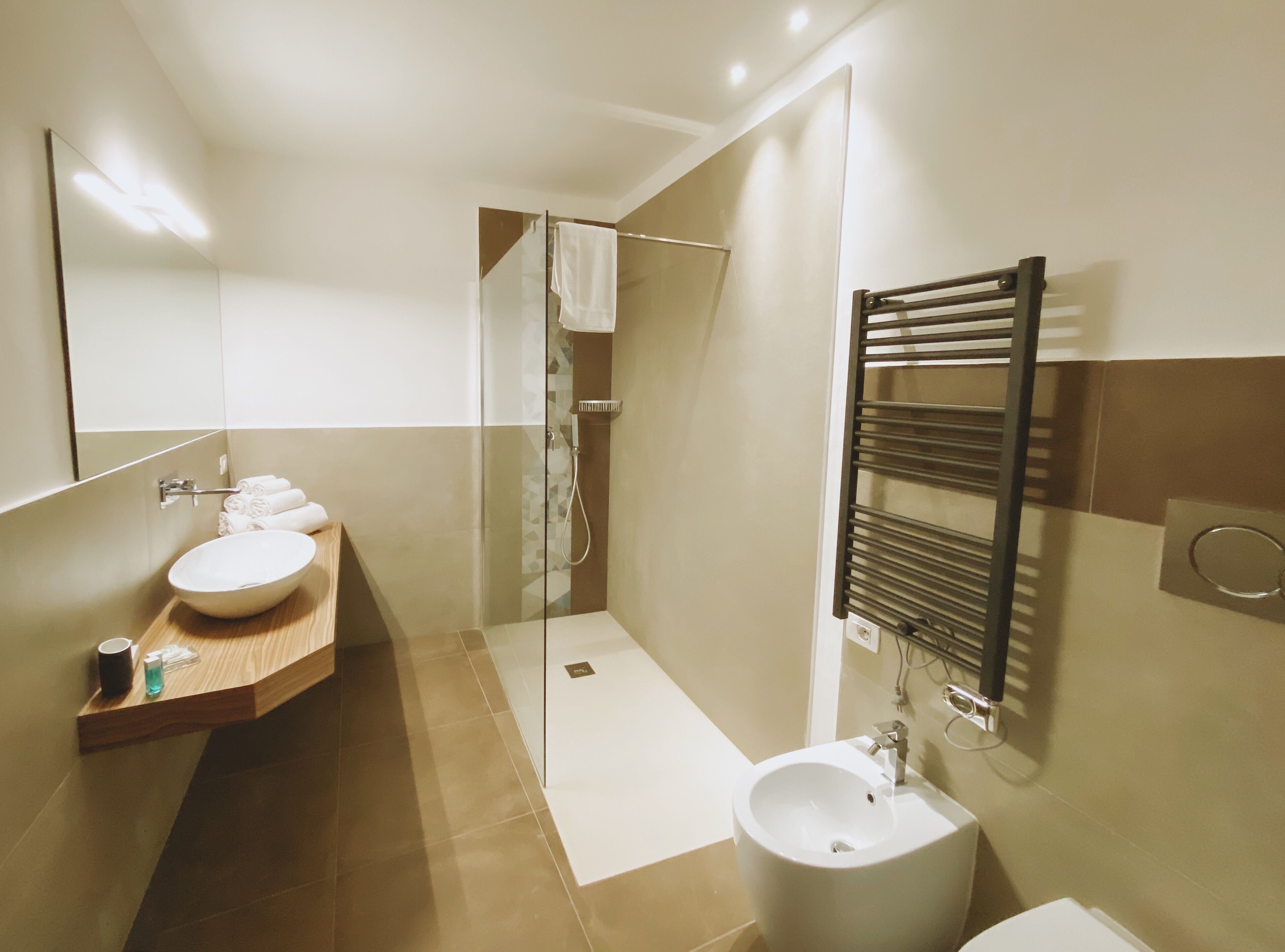A modern bathroom with a large mirror, a wooden vanity, a sink, a bidet, and a glass-enclosed shower.