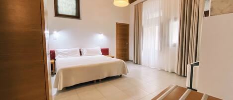 Quarto com cama, teto de madeira, janela com cortinas e luminária.