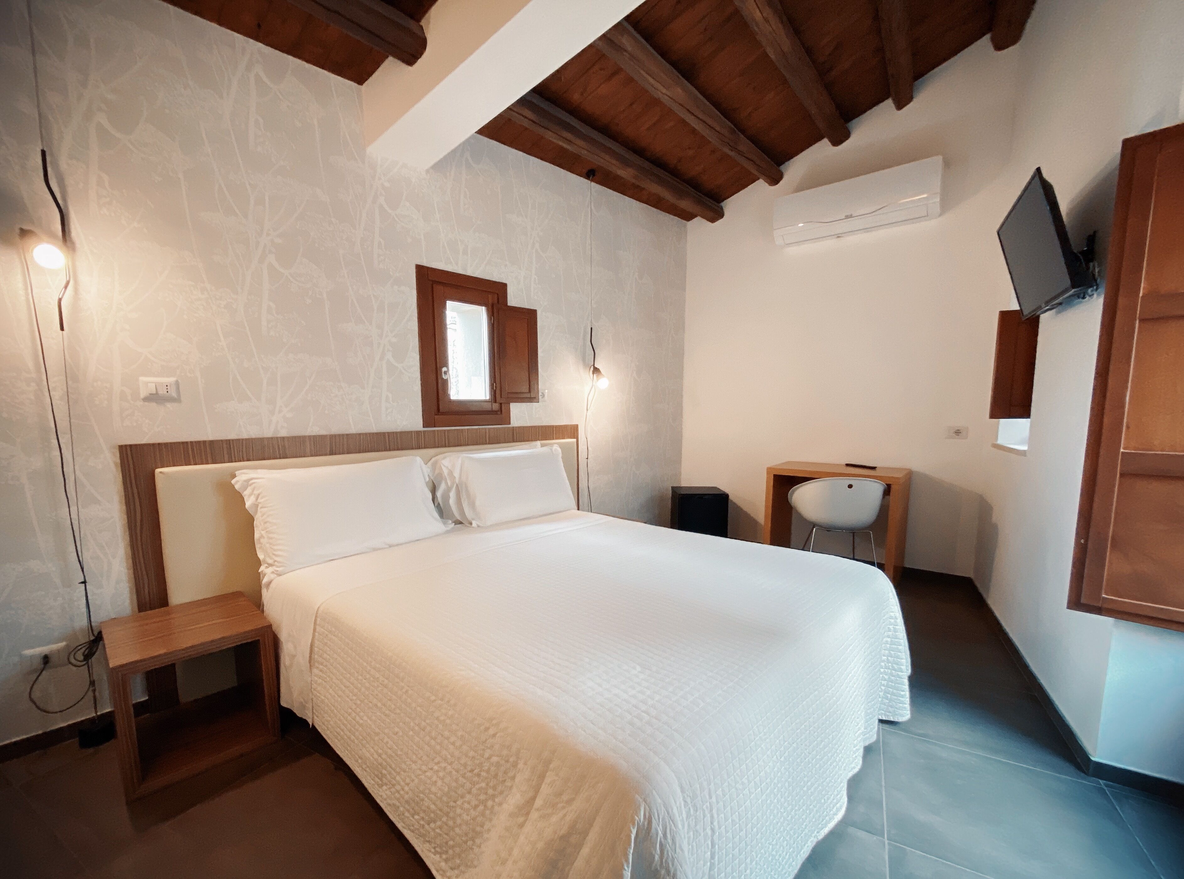 Une chambre à coucher comprenant un lit, une table de chevet, une chaise, un téléviseur fixé au mur et une fenêtre.