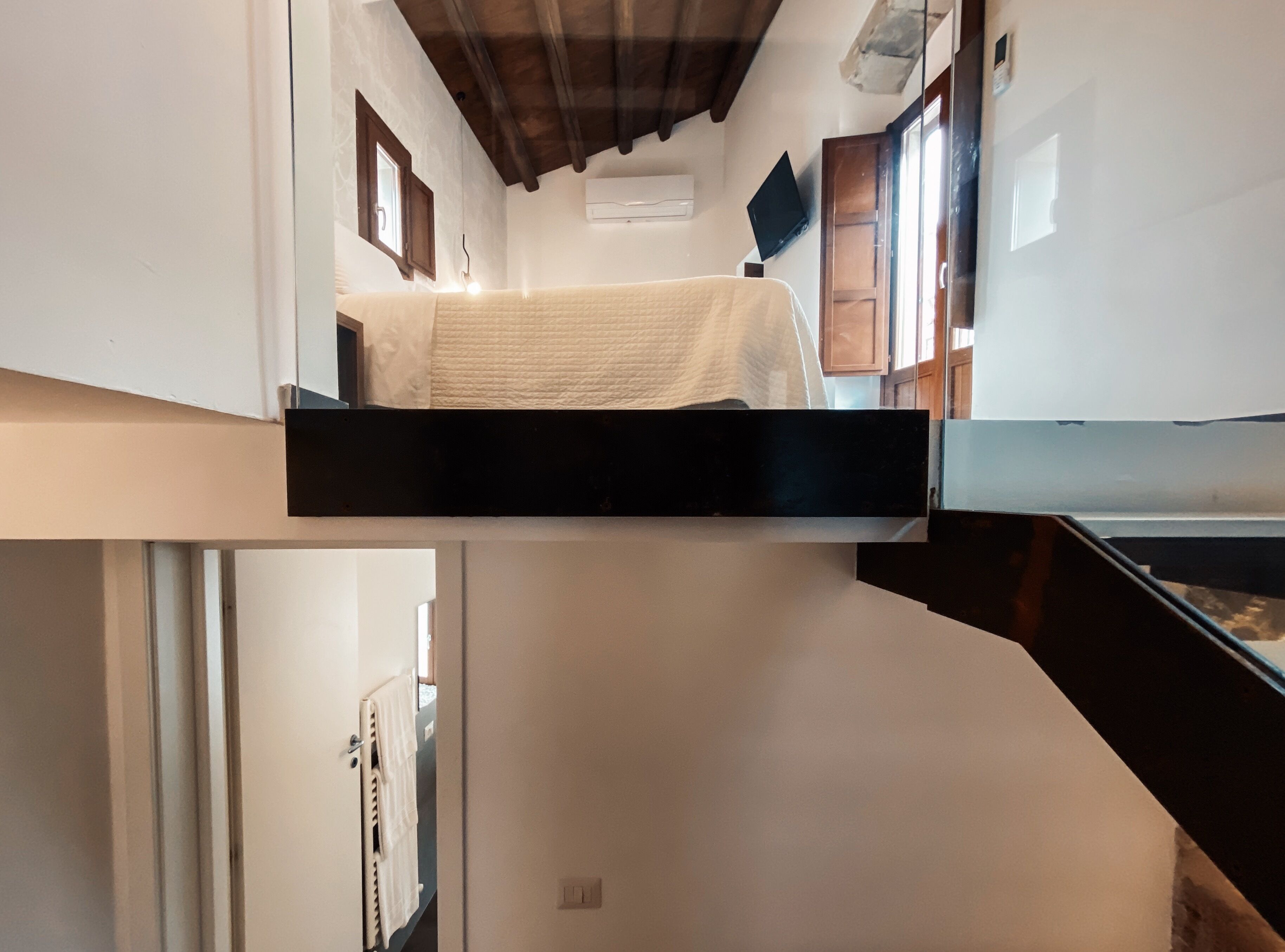 A bunk bed with a white mattress, a wooden ceiling, and a small window.