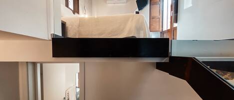 A bunk bed with a white mattress, a wooden ceiling, and a small window.