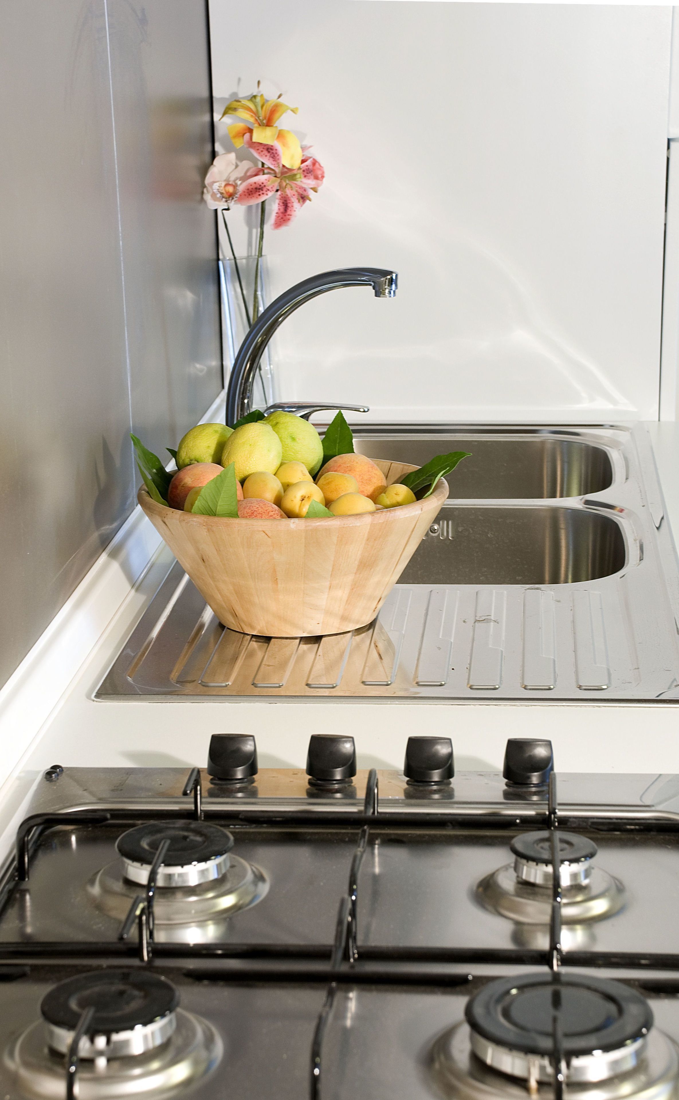A kitchen with a stove, sink, and a wooden bowl of fruit.