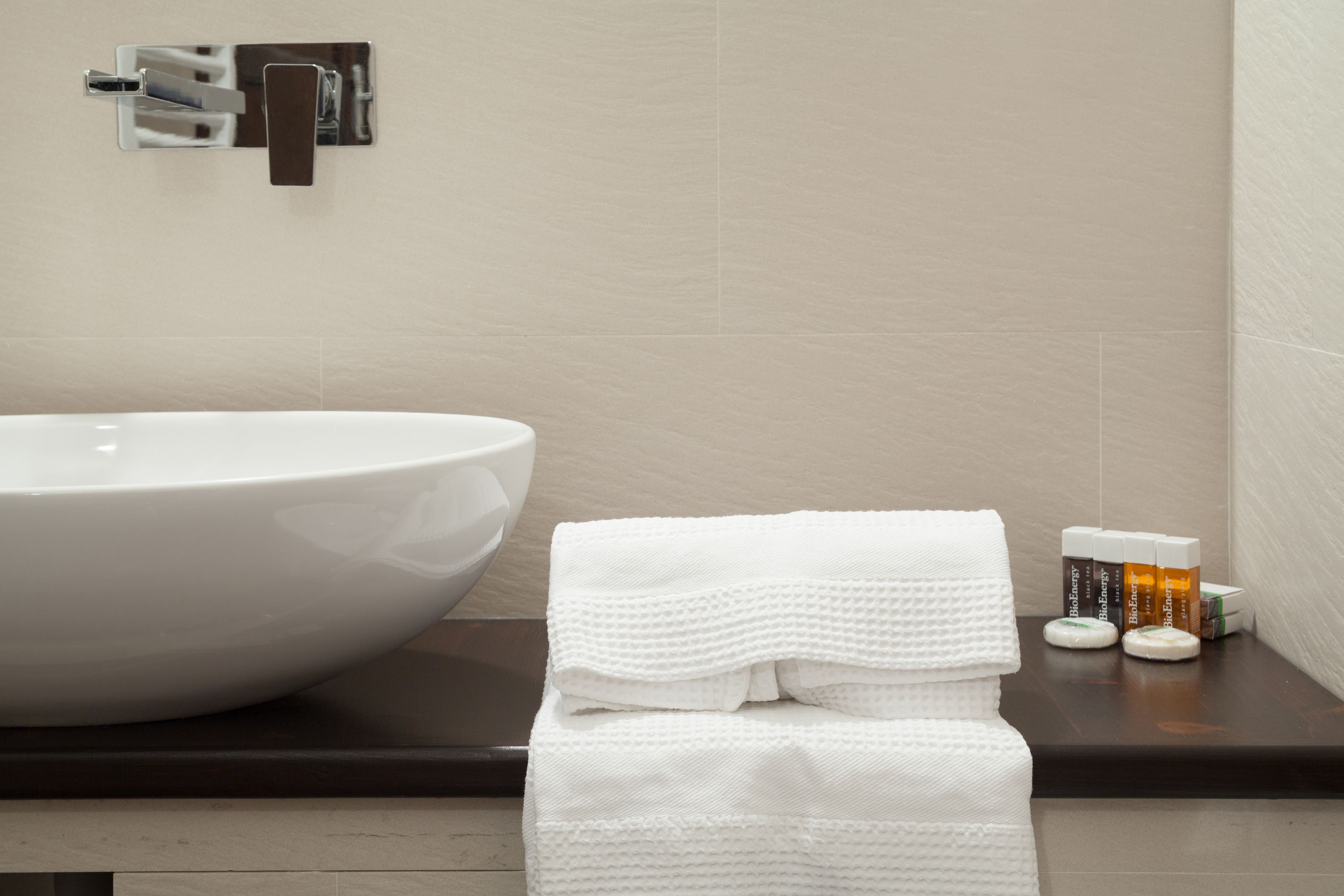 A bathroom with a large white sink, a towel rack with folded towels, and a small shelf with toiletries.