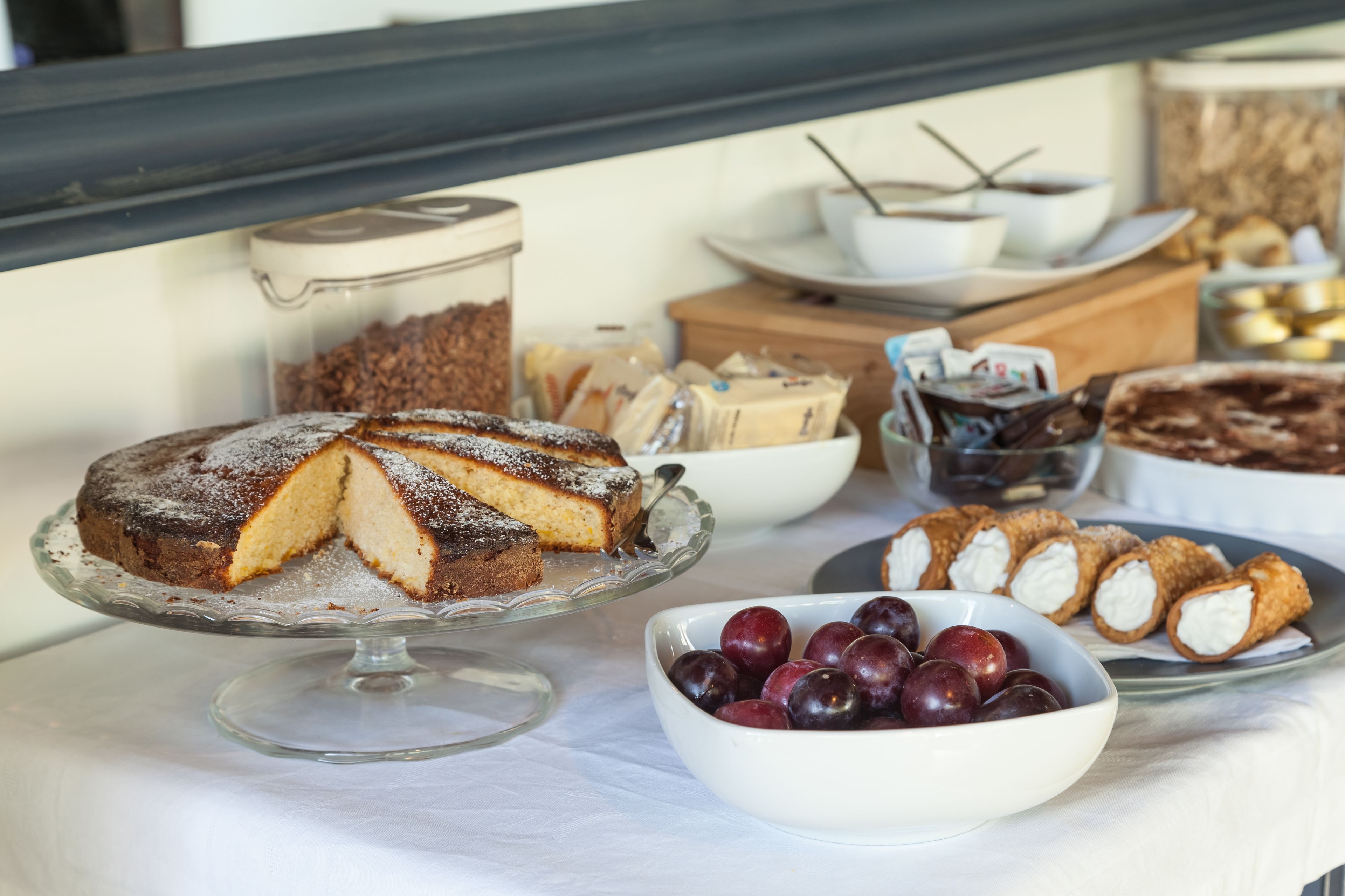 A buffet table with various desserts including a cake, pastries, and a bowl of plums.