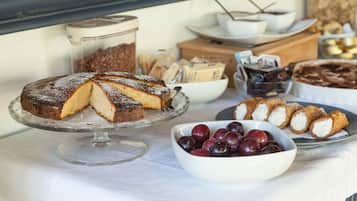 A buffet table with various desserts including a cake, pastries, and a bowl of plums.