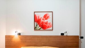 A bedroom with a wooden headboard, a bed with a yellow blanket, a framed picture of red flowers on the wall, and two bedside tables with lamps and a clock. - Locanda da Marco (Pignone)