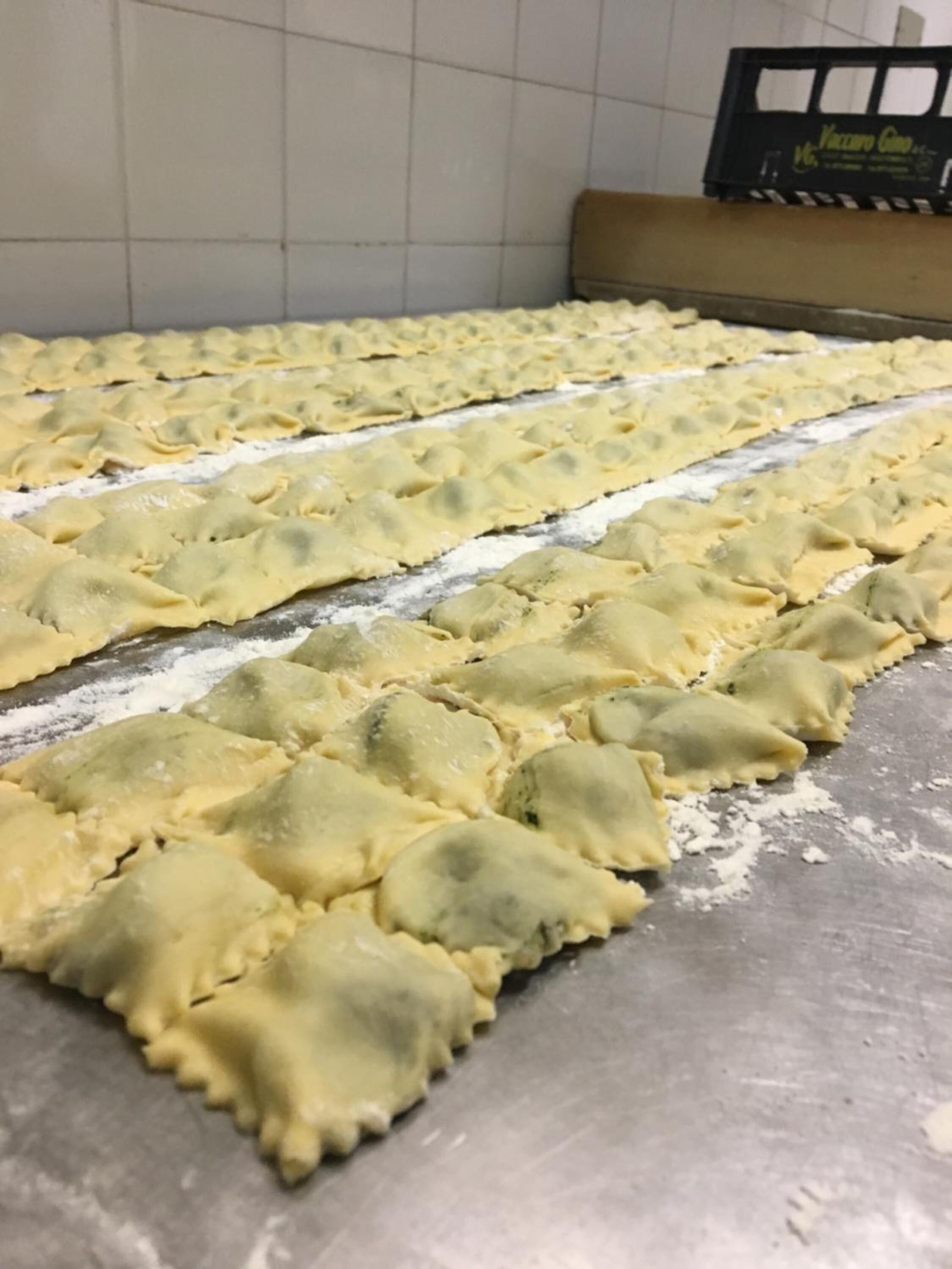 Una cucina con un'ampia superficie metallica ricoperta di farina, e una scatola con la scritta "Vincampo Cia" sullo sfondo.