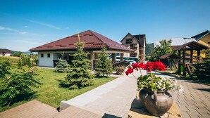 A residential area with a house featuring a red roof, a paved pathway, and a wooden bench with a potted plant. - Pensiunea Casa Humor (Gura Humorului)