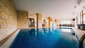An indoor swimming pool with stone walls and a clear blue pool, surrounded by a seating area with a view of the outdoors. - Pensiunea Casa Humor (Gura Humorului)