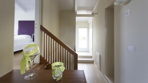A hallway with a wooden staircase, a bed in the background, and a table with two glasses and a bottle.