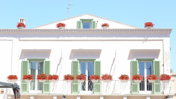 A white building with green shutters and flower boxes on the balcony.