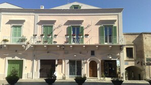 A two-story building with a balcony, green shutters, and potted plants.