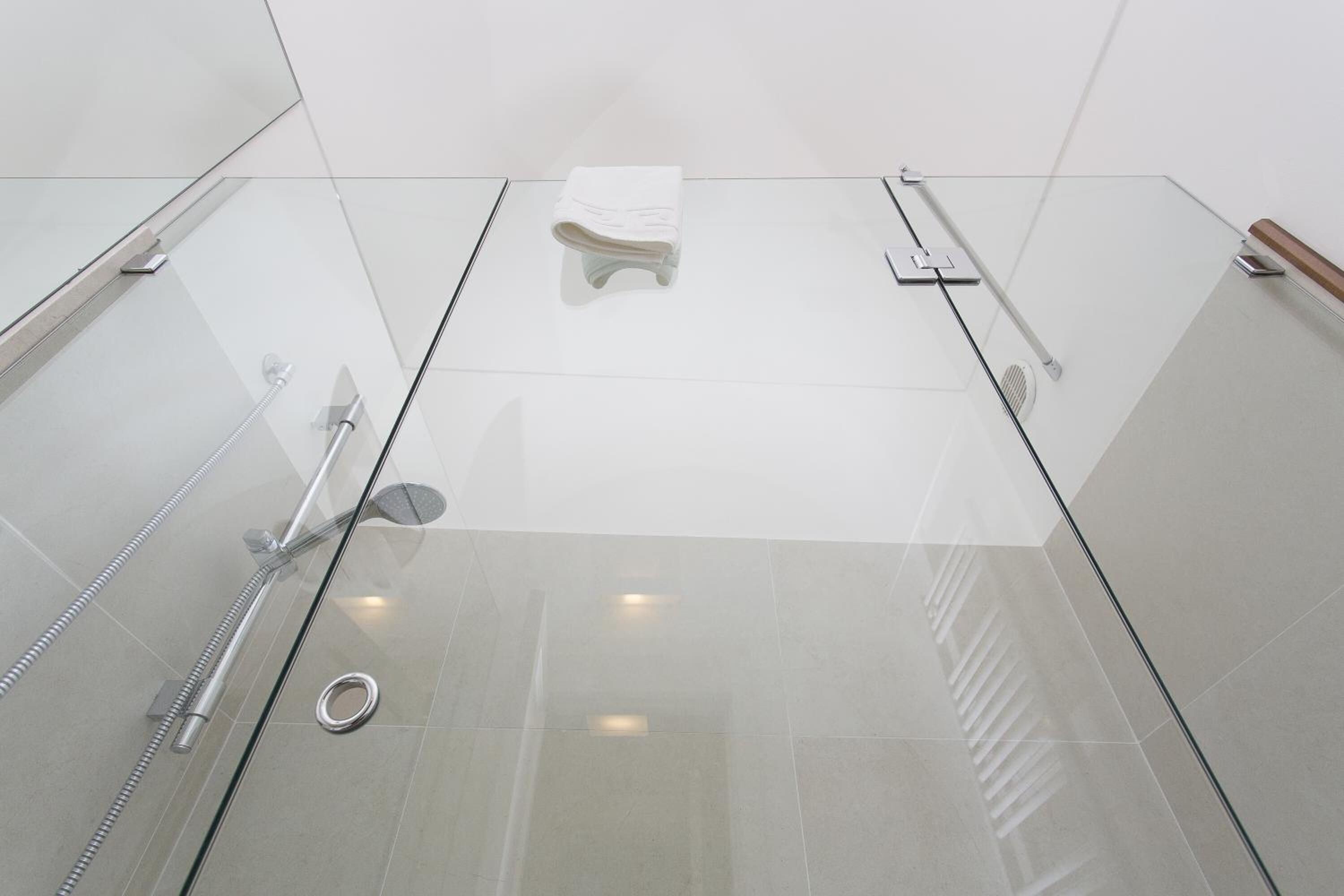 A modern shower area with glass walls, a white towel, and a handheld showerhead.