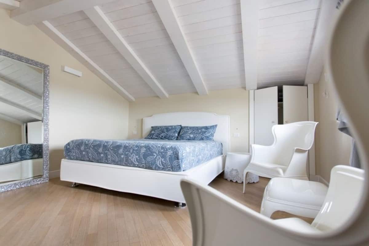 Ein Schlafzimmer mit einem Bett, einem Sessel, einem Spiegel und einem Kleiderschrank.
