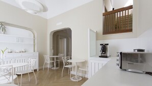 A modern kitchen with white cabinetry, a coffee machine, and a dining area with white chairs and tables.